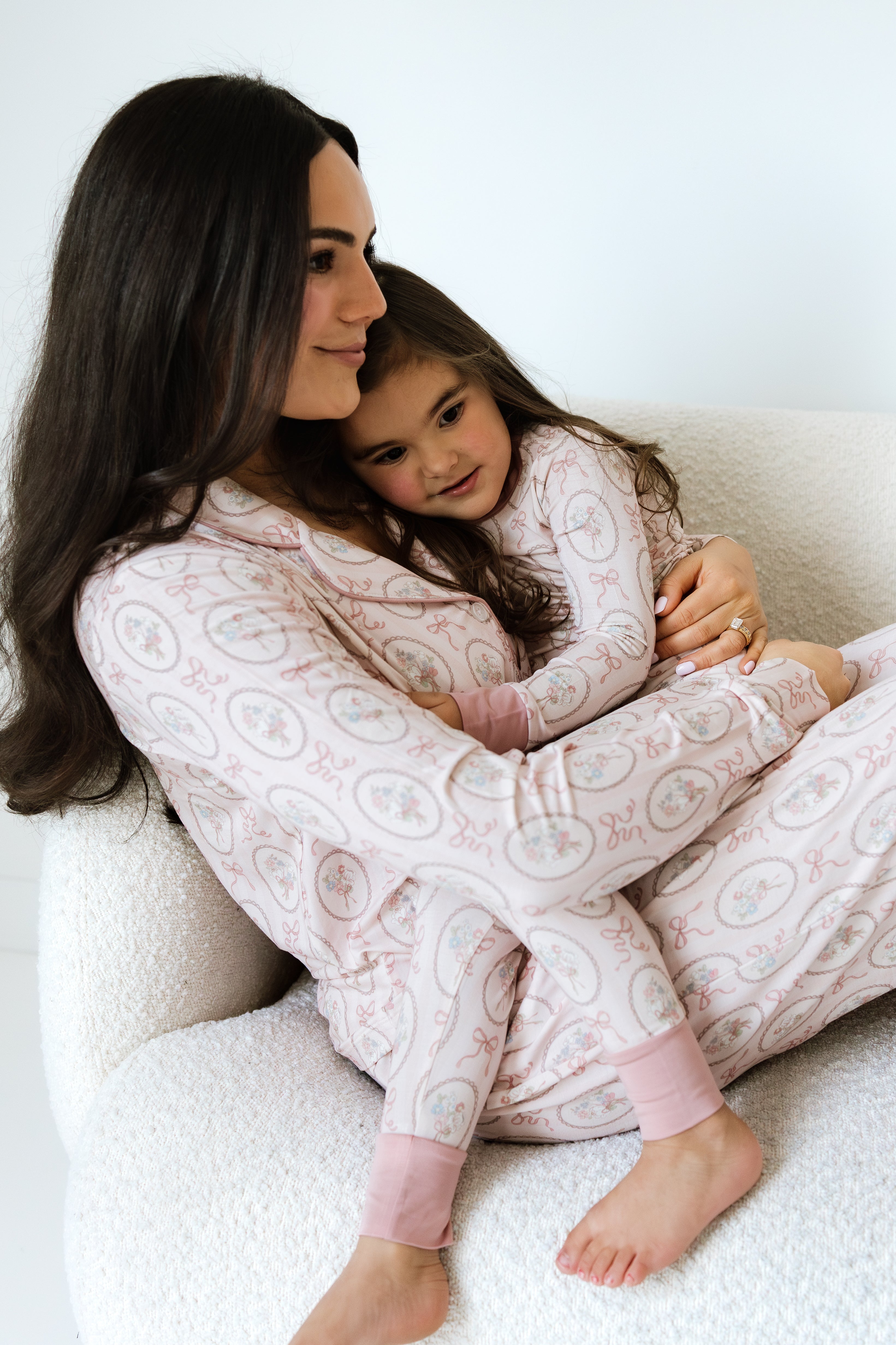 Woman and child sitting on a white couch wearing matching pajamas.