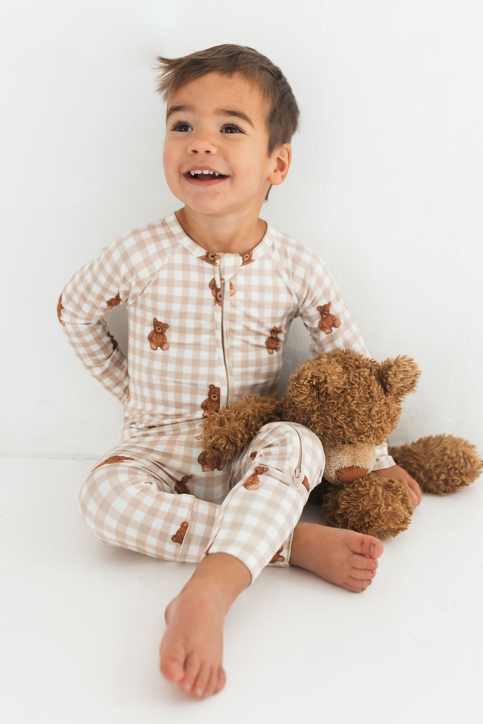 Child wearing checkered pajamas with a teddy bear on a white background